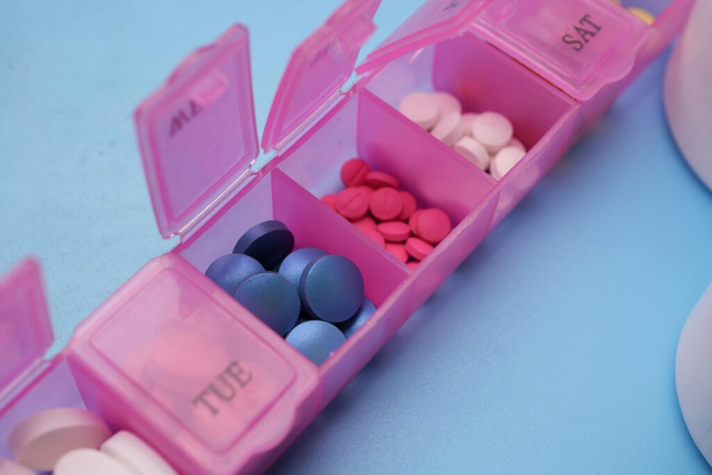 Pink pill organizer with colorful tablets arranged for weekly medication management.